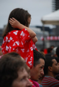 A child on a parent's shoulders, with hands over her ears.