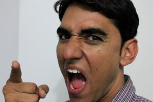 Angry man with open mouth and pointed index finger.