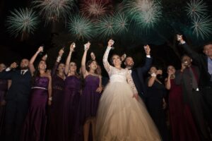 A bunch of people dressed in wedding attire, arms raised.