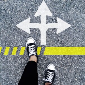 A person's feet by arrows painted on the road, indicating that they can go forward, left, or right.