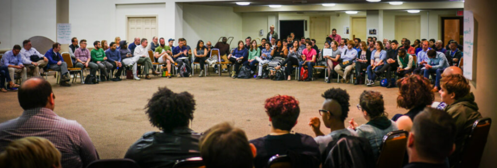 People sitting in a circle at a meeting in a large auditorium.