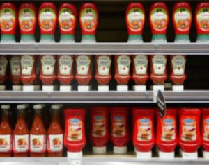 Multiple bottles and brands of ketchup on store shelves.