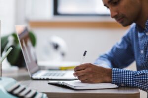 A man with a laptop and open notebook.