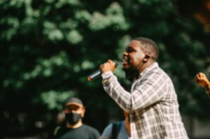 A man holding microphone and speaking outside.