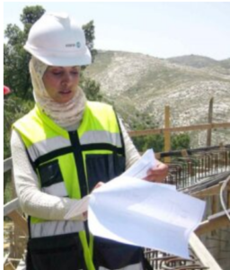 A construction worker reviewing written plans at a jobsite with a mountain in the background.