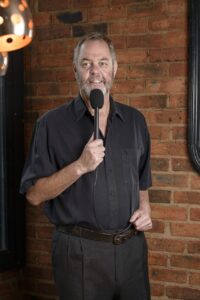 A man with smile, speaking into a microphone.