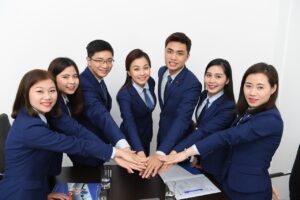 A team of Asian businesspeople, dressed in dark blue suits, each with one arm extended out toward the camera.