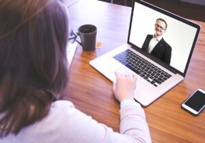 A woman at a desk in office and a man on computer screen.