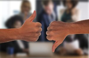 Two hands, one with thumb up and one with thumb down, in front of a small group which is blurred in the background.