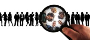A diverse group of faces shown under a magnifying glass, with silhouettes of people in the background.