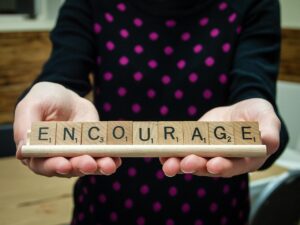 A person holding scrabble tiles on a scrabble tray; tiles spell the word "encourage."