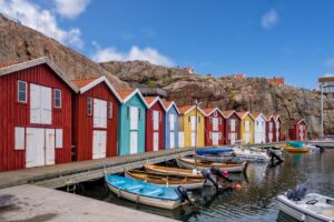 Different colored sheds in front of a body of water, with boats attached to the sheds.