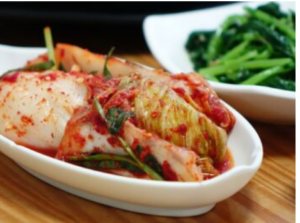 A Kimchi dish served next to a dish of green beans on a table.