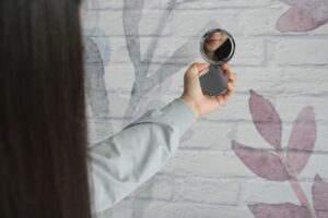 Person holding out hand with a mirror, looking in the mirror.