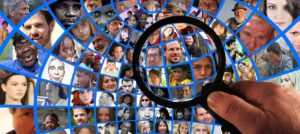 Magnifying glass highlighting some faces out of many diverse faces on a globe.